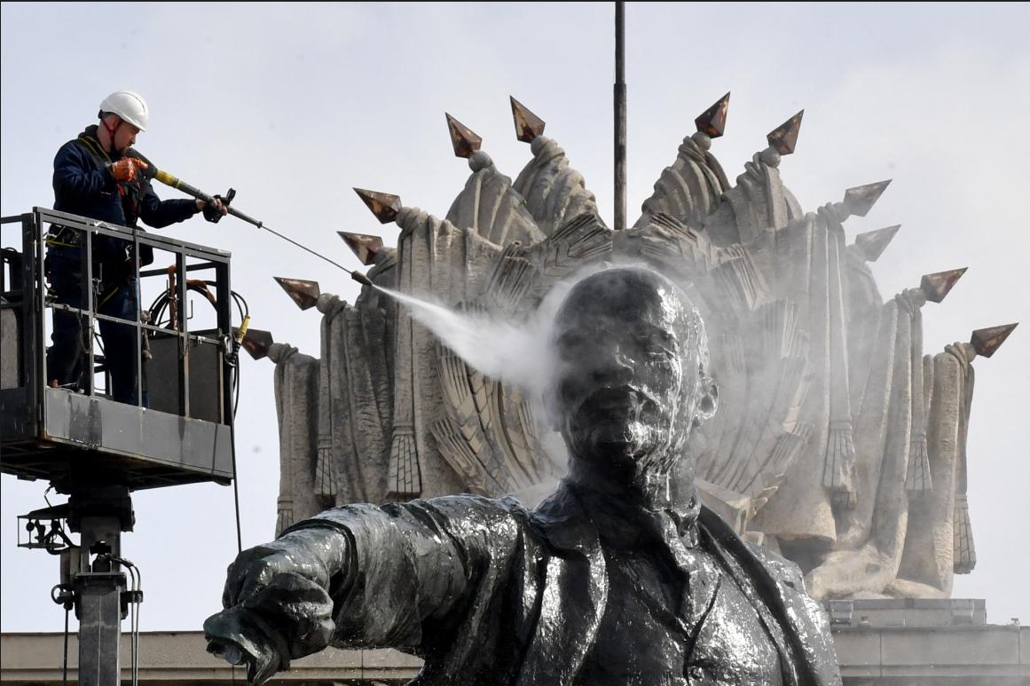 Un homme juché sur une grue nettoie avec un karsher une statue imposante de Lénine