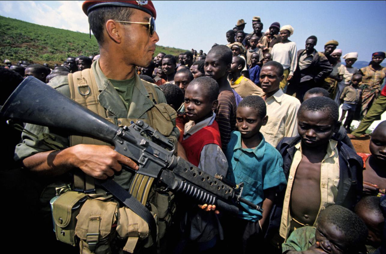 Un militaire avec une arme de guerre devant une foule d'enfants et d'adultes