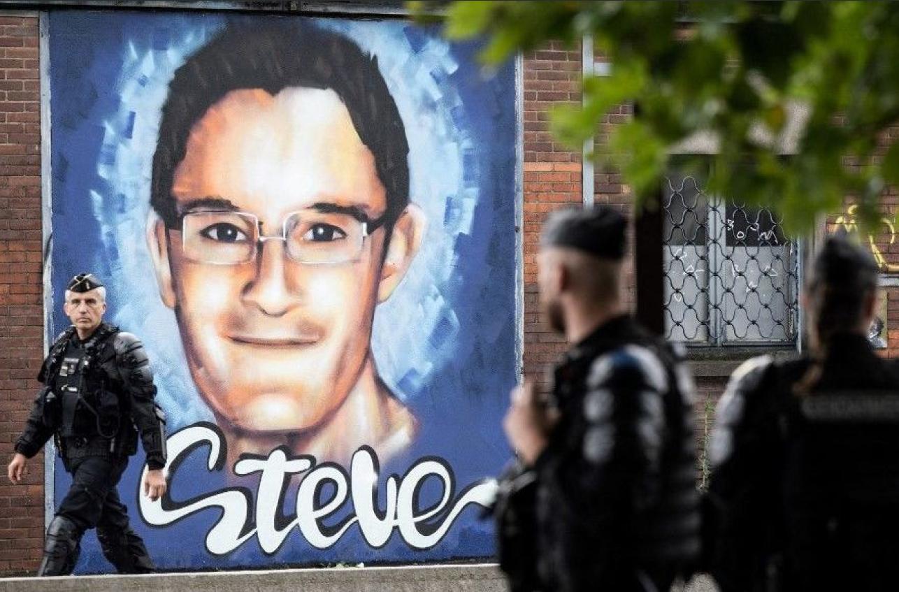 Des policiers devant une affiche de Steve de plusieurs métres de haut collée sur un mur